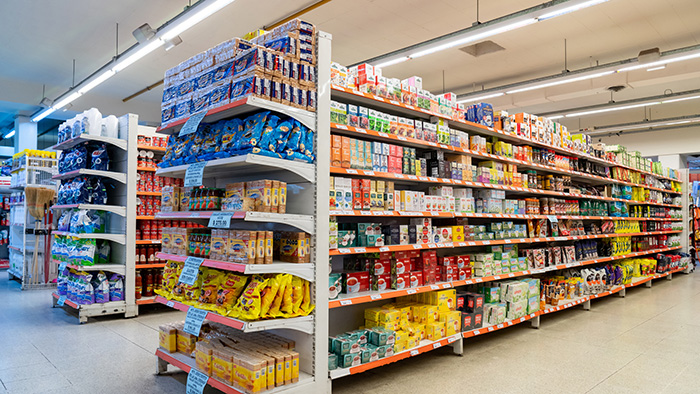 Grocery store aisle with shelves of packaged food products under bright lighting.